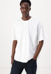 Hvid bomulds t-shirt med afslappet pasform, rund hals og korte ærmer. Kombineret med mørke denim jeans. Subtilt logo ved sømmen.