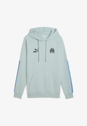 Gaiši mentolzaļa kapuce ar kangoru kabatu. Melna "Puma" logo, uzkrītošs "KING" teksts un "OM" simbols izdrukāti uz krūtīm. Zilā rakstainā akcenti uz piedurknēm.