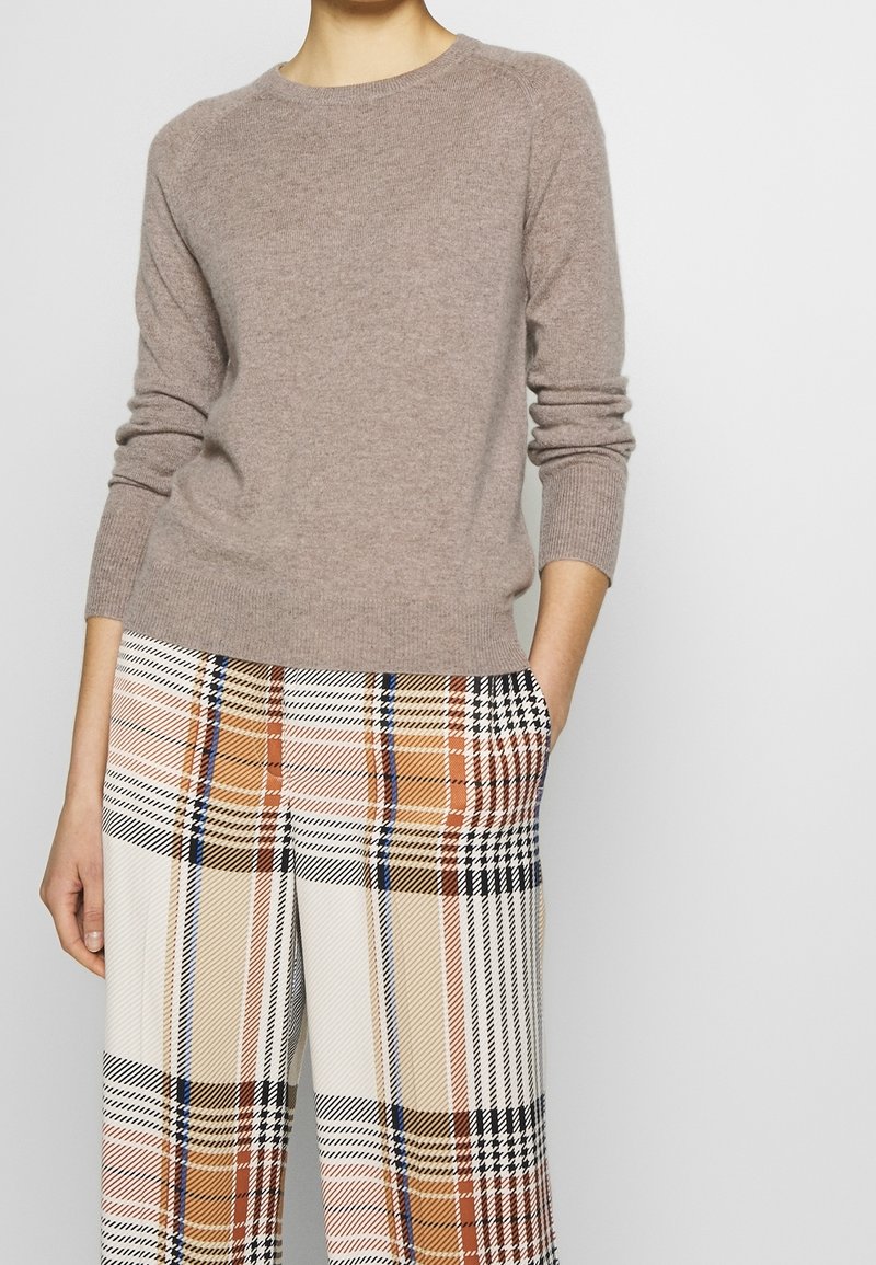 Pull en maille brun clair avec col rond et manches longues côtelées. Associé à un pantalon large à carreaux aux nuances d'orange, de noir et de crème.