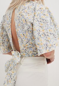 Haut floral cropped en tissu léger, avec des manches bouffantes, un dos ouvert et un détail à nouer à la taille. Les couleurs disponibles sont le jaune, le bleu et le vert.
