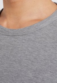 Grau gestreiftes Baumwoll-T-Shirt mit Rundhalsausschnitt und strukturiertem Oberflächenmaterial, das eine Nahaufnahme des Halsausschnitts und des oberen Brustbereichs zeigt.