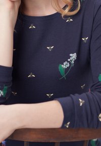 Námořnický modrý top s dlouhým rukávem a vzorem květin a včel. Měkký materiál, kulatý výstřih, s zelenými listy a bílými květinami.