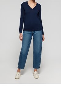 Pull en maille douce bleu marine à col en V, associé à un jean bleu taille mi-haute avec une coupe droite. Le mannequin porte des baskets blanches.