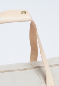 Borsa in tela beige con manico in pelle color beige chiaro, dotata di un bottone a pressione in ottone e di una zip dorata lungo la cucitura superiore.