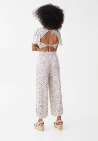 Bloemen jumpsuit met korte mouwen, open rug en striksluiting. Lichte stof met een losse pasvorm en wijde broekspijpen in pastelkleuren. Wedge sandalen.