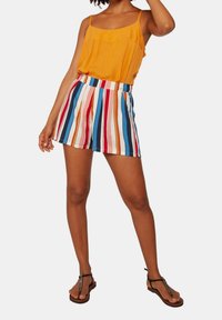 Orange sleeveless top and multicolored striped shorts with pockets. Shorts feature vertical stripes in red, blue, and beige. Black flip-flops.