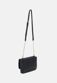 Borsa a tracolla nera trapuntata con catena staccabile e tracolla in pelle. Presenta una forma rettangolare e una texture liscia. Accenti in hardware dorato.