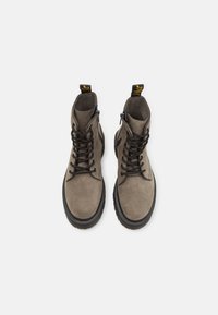 Botas de tobillo de ante gris con cordones negros, suela gruesa negra y una lengüeta en la parte trasera. Presenta un logo en relieve en la lengüeta.
