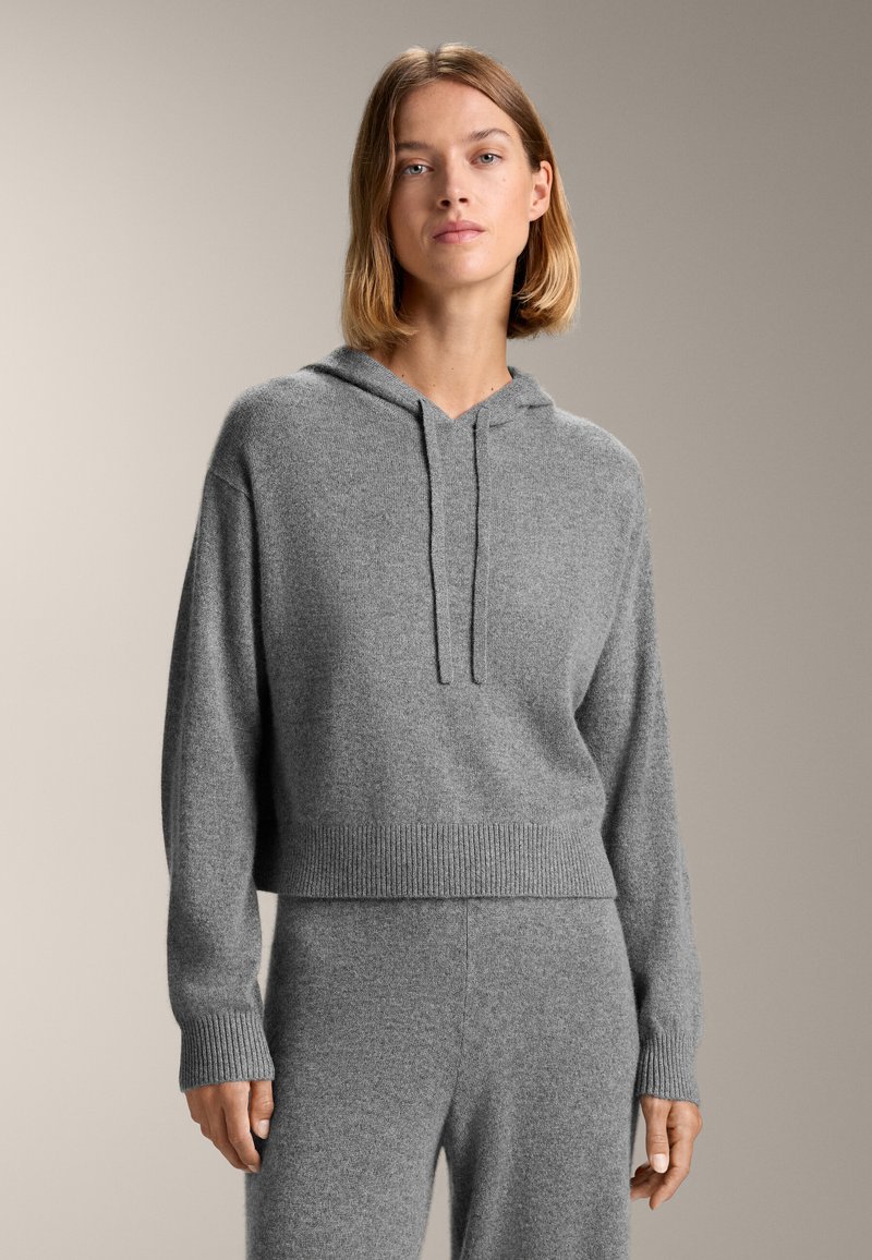 Felpa grigia corta realizzata in morbido tessuto a maglia, con cappuccio regolabile, polsini a coste e orlo, abbinata a pantaloni grigi coordinati.