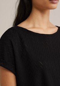 Must have tekstuuriga must ülemus, millel on lõtv istuvus, lai kaelus ja peen chevron muster. Pehme kangas koos rullitud varrukate detailidega.