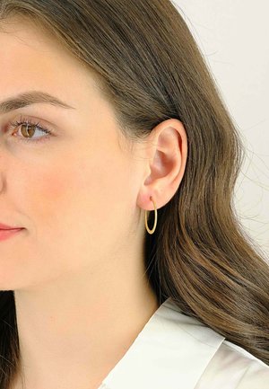 Orecchino a cerchio in oro indossato da un modello, caratterizzato da un design sottile ed allungato. L'orecchino ha una finitura liscia e lucida con una leggera brillantezza.