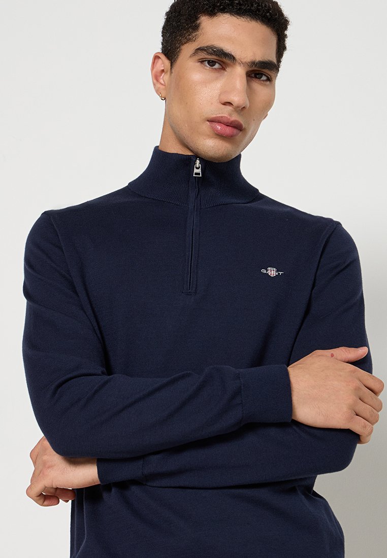 Granatowy sweter na zamek z wysokim kołnierzem, o miękkiej fakturze i dopasowanym kroju. Posiada małe logo na piersi oraz długie rękawy.