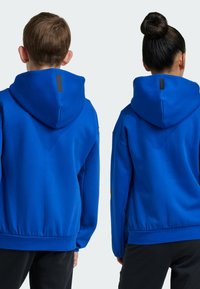 Blå huvtröja i mjukt tyg, med ribbad fåll och en svart märkesetikett på baksidan. Finns i en avslappnad passform.