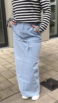 Saia maxi de ganga azul clara com corte reto, bolsos laterais e passante para cinto, vestida com uma blusa de manga longa com riscas pretas e brancas.