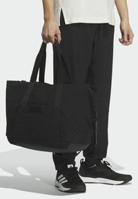 Borsone in tessuto nero con doppie maniglie, chiusura a zip e una tasca frontale. Presenta una superficie texture e una lieve lucentezza.