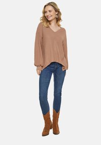 Hellbraunes, geripptes Strick-Pullover mit V-Ausschnitt, Ballonärmeln und abgerundetem Saum, kombiniert mit dunkelblauen Skinny Jeans und hellbraunen Wildlederstiefeln.