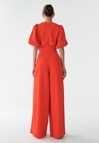 Punane ülikond puffvarrukatega, istuv talje ja laiad püksid. Valmistatud siledast kangast, millel on õrn sära.