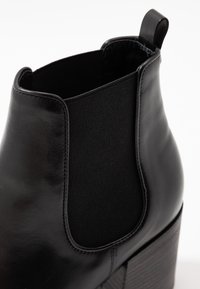 Stivale alla caviglia in pelle nera con pannello laterale elastico, punta arrotondata e tacco a blocco testurizzato. Finitura liscia con dettagli di cucitura a contrasto.