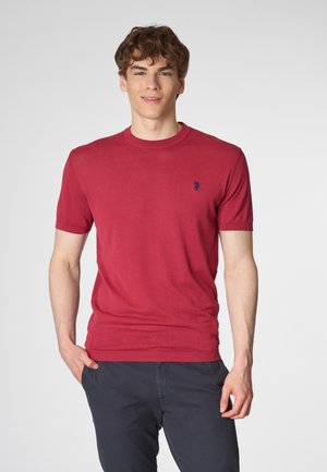 Pullover rosso a maniche corte realizzato in tessuto leggero, con colletto rotondo e un piccolo emblema blu sul lato sinistro del petto.