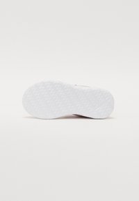 Weiße Sneaker-Sohle mit strukturiertem Grip-Muster und glatten, abgerundeten Kanten, die ein dezentes Logo-Motiv nahe der Ferse zeigt.