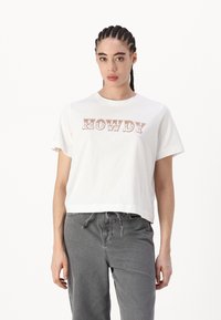 Bílý zkrácený tričko s nápisem "HOWDY" v hnědém, hravém písmu. Vyrobeno z měkké bavlny s kulatým výstřihem a krátkými rukávy.