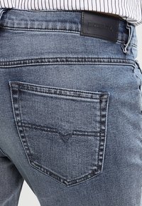 Los vaqueros de mezclilla azul oscuro presentan un diseño de bolsillo trasero en forma de V distintivo, costuras en contraste y un parche de cuero de la marca en la cinturilla.