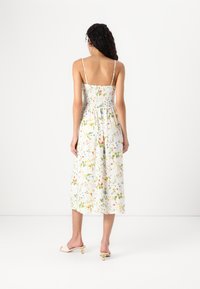 Φλοράλ μίντι φόρεμα από ελαφρύ ύφασμα με σμιχτό πίσω μέρος, λεπτές τιράντες και λευκό φόντο που έχει πολύχρωμα λουλουδάτα σχέδια.