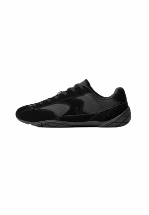 Chaussure de sport noire avec un mélange de matériaux en daim lisse et texturé. Caractéristiques : profil bas, design à lacets, et semelle en caoutchouc avec motifs de traction.