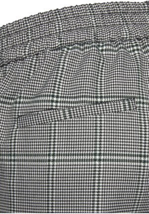 Gros plan sur un tissu noir et blanc à motif pied-de-poule et tartan, avec une ceinture élastique froncée et une poche fendue horizontale.