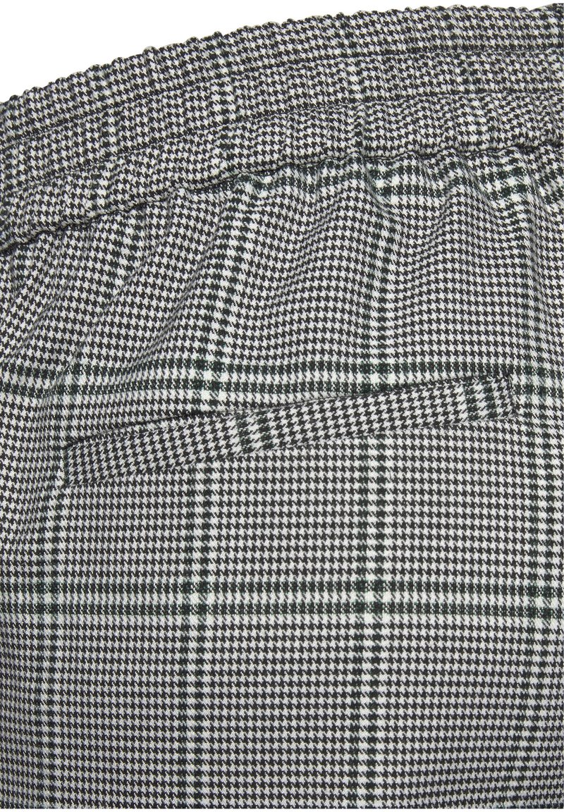 Gros plan sur un tissu noir et blanc à motif pied-de-poule et tartan, avec une ceinture élastique froncée et une poche fendue horizontale.
