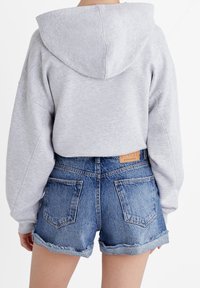 Hoodie harmaa, jossa on vetoketjullinen huppu, yhdistettyinä farkkushortseihin, joissa on revitty helma ja takataskut, esittäen rentoa ja mukavaa tyyliä.