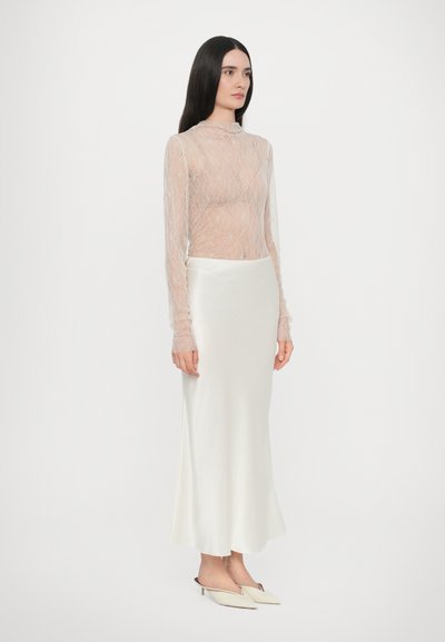 Top trasparente a maniche lunghe con motivo geometrico, abbinato a una maxi gonna in satin bianco liscia. Le calzature hanno la punta affusolata e tacco basso.