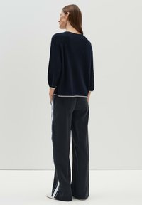 Navy gestrickter Pullover mit Dreiviertelärmeln, kombiniert mit schwarzen, weit geschnittenen Hosen, die an den Seiten weiße und blaue Streifenakzente haben.