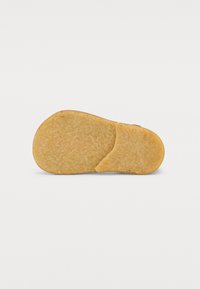Semelle de chaussure en caoutchouc beige, présentant une surface texturée avec une forme arrondie et une indentation irrégulière d'un côté.