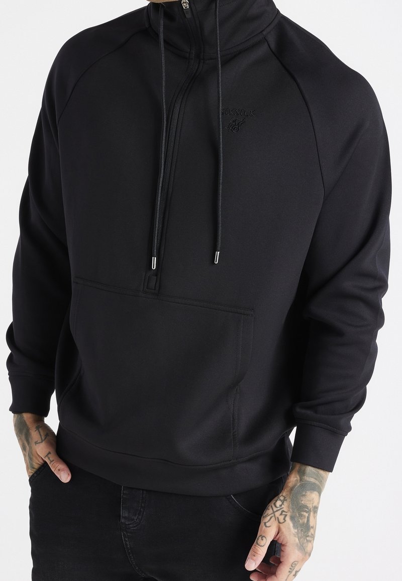 Pullover nero con zip al collo realizzato in un materiale liscio e elasticizzato. Presenta una tasca frontale, cordini regolabili e polsini a costine.