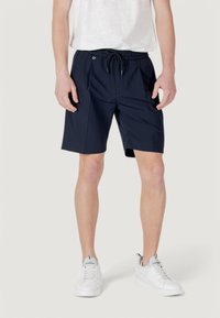 Shorts blu navy realizzati in tessuto leggero, con vita elasticizzata e cordino, e tasche laterali. Indossati con sneakers bianche.