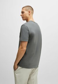 T-shirt gris à manches courtes avec un col rond, texture lisse et coupe décontractée, associé à un pantalon clair.