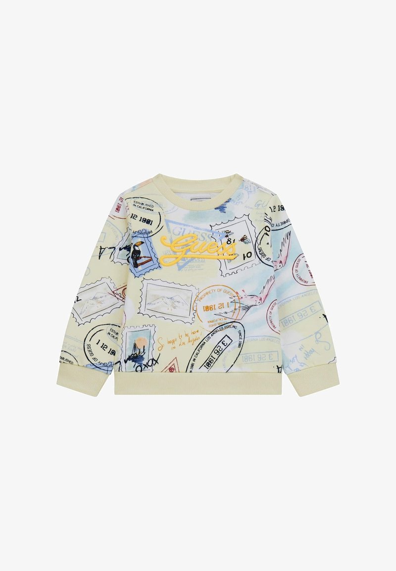 Sweat-shirt crème avec un timbre-poste coloré et des imprimés sur le thème du voyage, avec un logo "Guess" jaune brodé sur la poitrine.