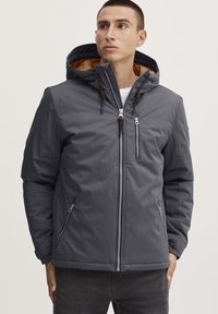 Gray insulated jacket with a zippered front, adjustable hood, and two side pockets. Features contrasting brown inner lining and decorative drawstrings.