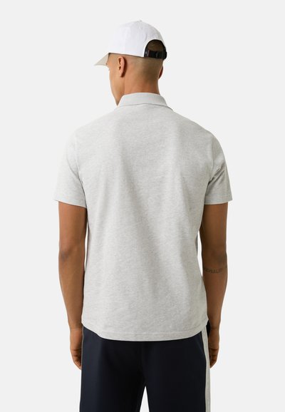 Hellgraues kurzärmliges Poloshirt aus Baumwolle mit klassischem Kragen und lässiger Passform, von hinten betrachtet, getragen mit dunkelblauen Hosen.