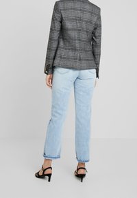 Grå rutiga kavaj med strukturerade axlar, tillsammans med ljusblå raka jeans och svarta remsandaler. Texturerad tyg och rena linjer.