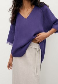 Haut violet en lin avec col en V, manches courtes et bords effilochés, assorti à une jupe beige clair avec une taille nouée.