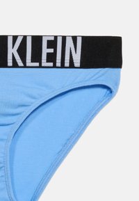 Φωτεινό γαλάζιο σλιπ με φαρδιά μαύρη ζώνη μέσης που διαθέτει λευκό μερικώς ορατό κείμενο.