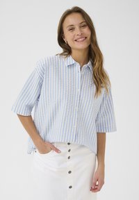 Short-sleeve button-up shirt in light blue and white striped cotton, featuring a classic collar and relaxed fit, paired with a white skirt.
