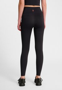 Svarta högmidjade leggings med en slät yta, med en smal midja och röda chevronaccenter på baksidan.