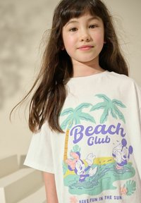 Witte katoenen t-shirt met een kleurrijke print van palmbomen en cartoonfiguren. De tekst luidt "Beach Club" met accentkleuren in paarse en groene tinten.