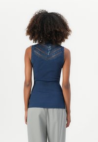 Top sem mangas em azul marinho com textura canelada, apresentando um design de costas rendadas e uma silhueta ajustada, a combinar com calças listradas em cinza claro.