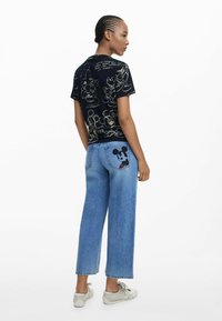 Zwarte t-shirt met korte mouwen met prints van cartoonfiguren; gedragen met lichtblauwe wijde jeans met een Mickey Mouse-patch op de achterzak.