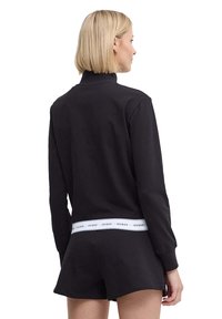 Sudadera corta negra con cuello alto, que presenta una banda de logo blanca en la cintura y mangas largas. Tejido suave y corte relajado.