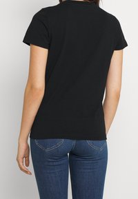 Camiseta de algodón negra con manga corta, diseño ajustado, cuello redondo y textura suave, combinada con jeans de mezclilla azules que cuentan con bolsillos traseros.